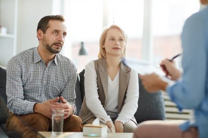 Young couple sitting on couch in front of psychologist and listening to her advice at meeting